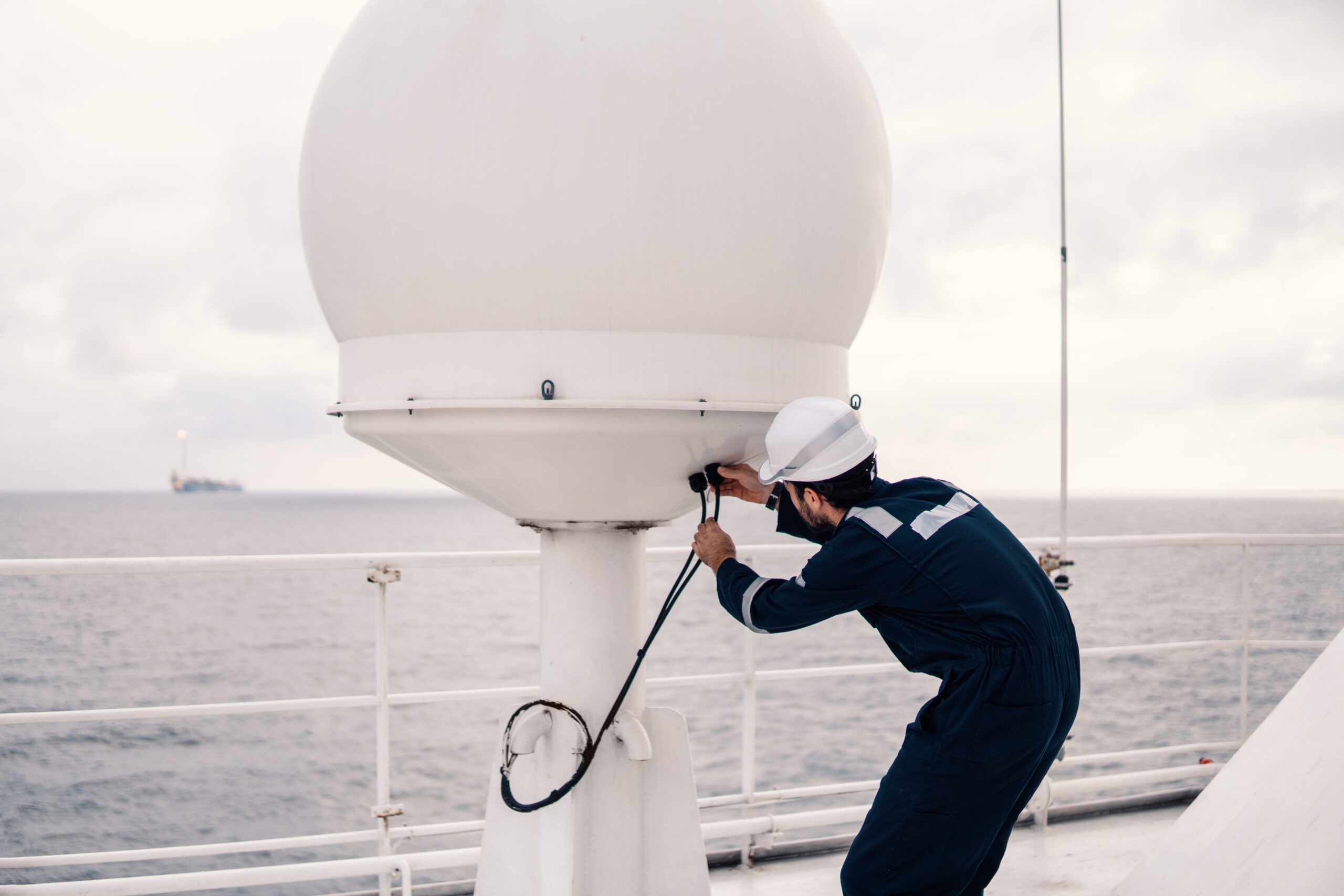 Marine service technician or serviceman repairing VSAT terminal on deck of vessel or ship. He is checking connection cables
